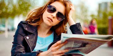 Adult child of divorce wears glasses and looks serious on a park bench with a paper