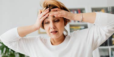 Portrait of a woman with her hands on her forehead, capturing the deep exhaustion and internal conflict described by parents of Gen-Z and Gen-Alpha teens.