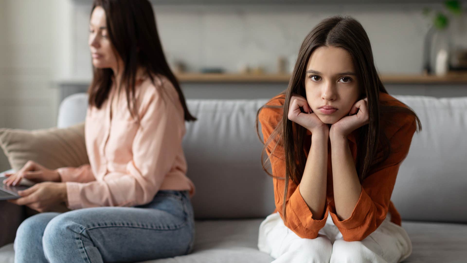 Teen Gen Z daughter looks annoyed and upset with her mom in the background