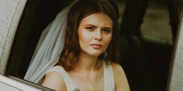A bride in a wedding dress looking out of a car window.