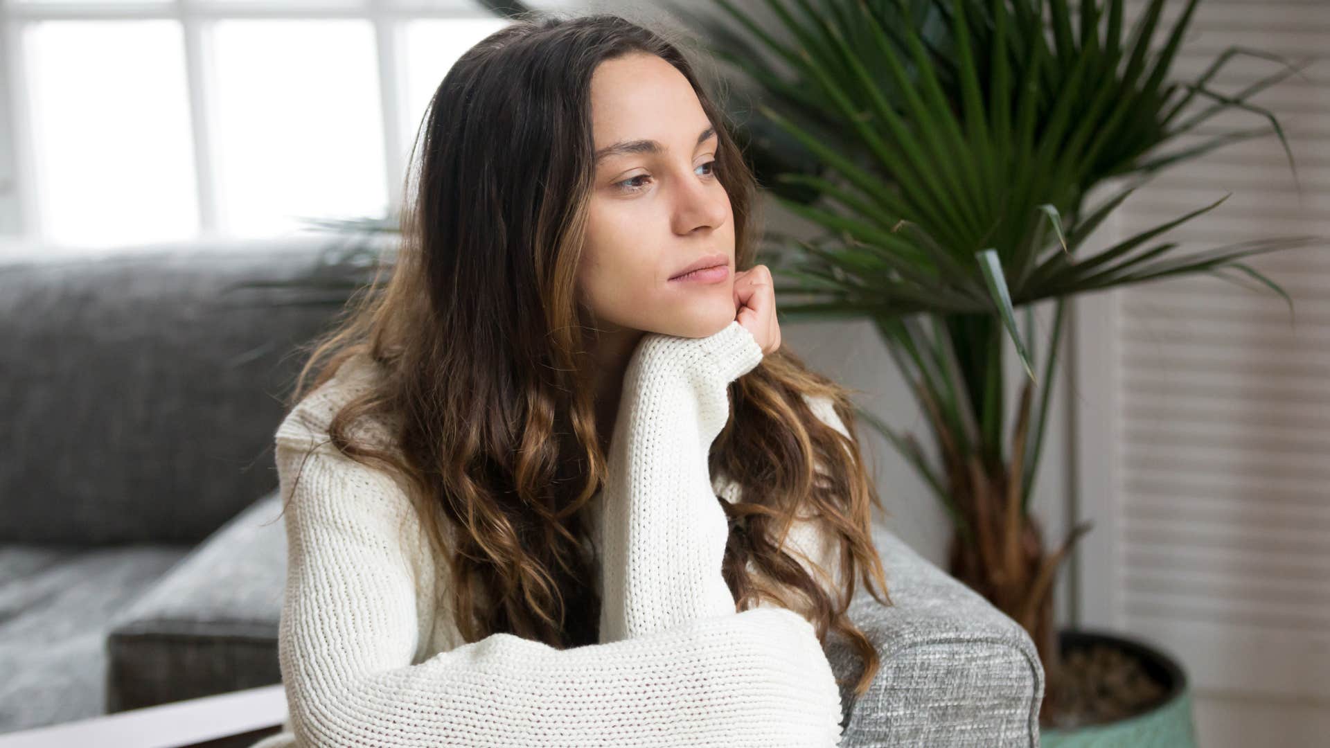 woman in white sweater looking out the window as she thinks it's whatever i'm over it