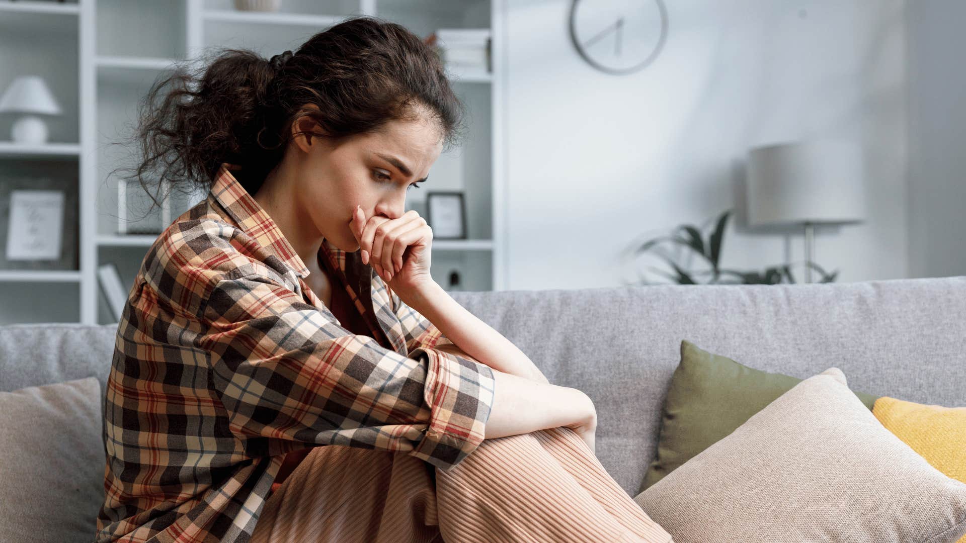 Gen Z woman whose parents were emotionally distant looks stressed on a couch 