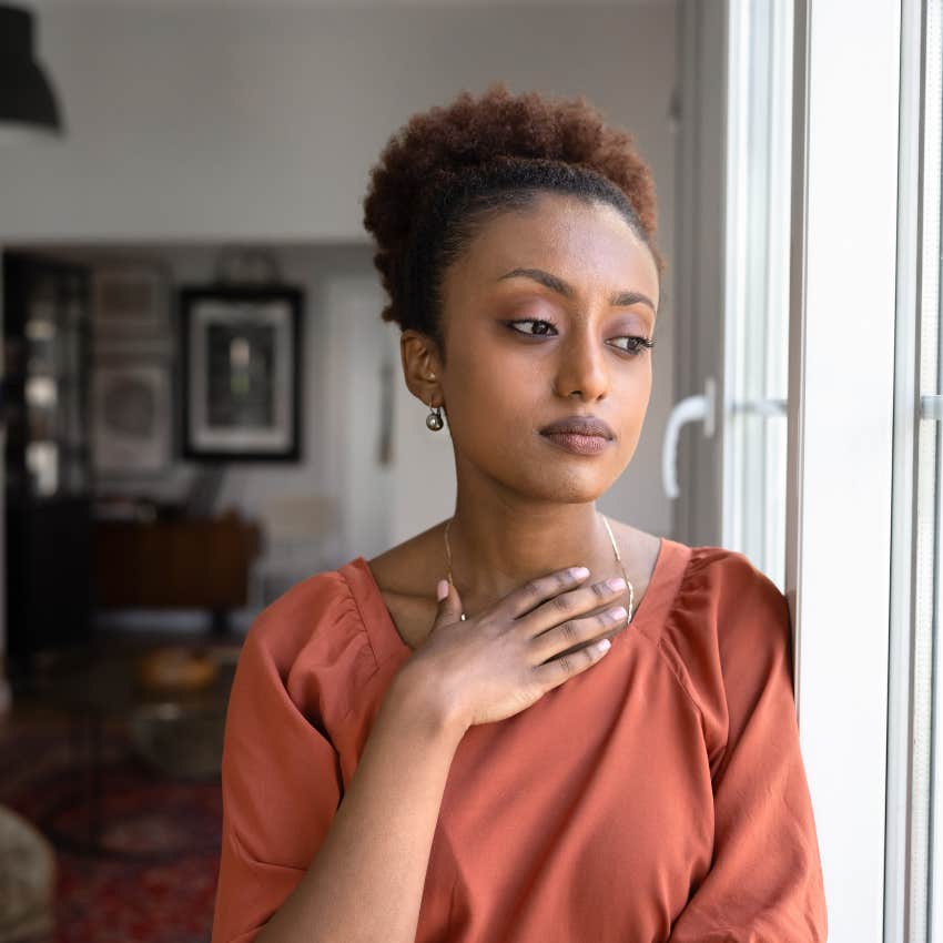 upset black woman standing near window at home